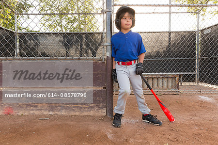Boy leaning against fence with baseball bat at practise on baseball field