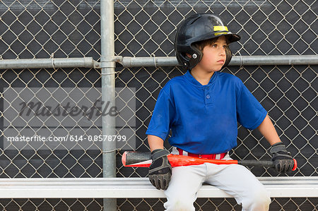Boy with baseball bat watching from bench at baseball practise
