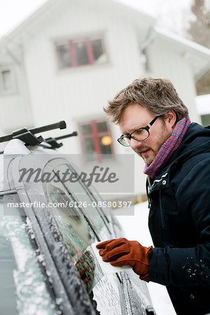 Sweden, Vastra Gotaland, Olofstorp, Man scraping ice off car window