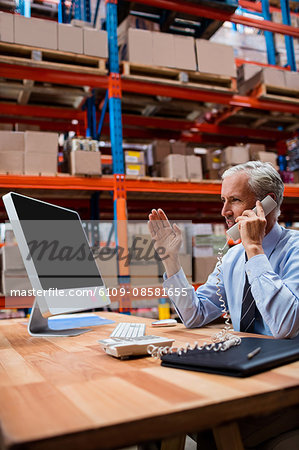 Warehouse manager using a laptop talking on the phone
