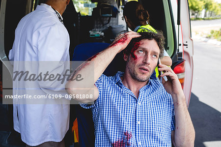 Injured man on the phone with ambulance men behind