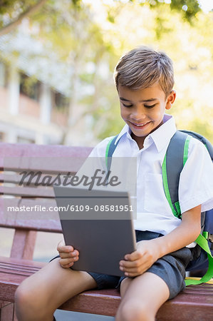 Schoolboy sitting on bench and using digital tablet in campus