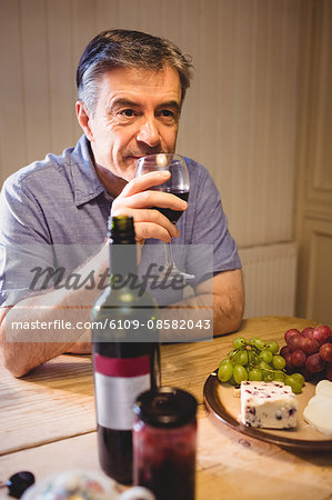 Mature man sitting at table and tasting red wine