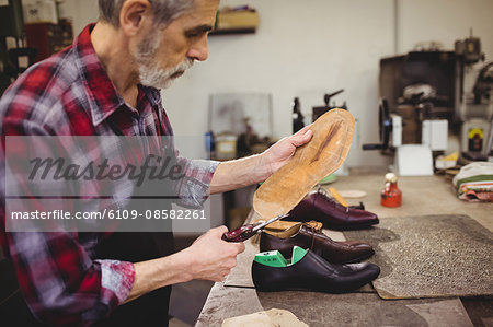 Profile view of cobbler cutting the sole of a shoe