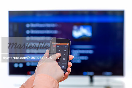 Closeup on woman hand holding smartphone and use a app with remote control  and surfing programs on television. Focus on the remote control.