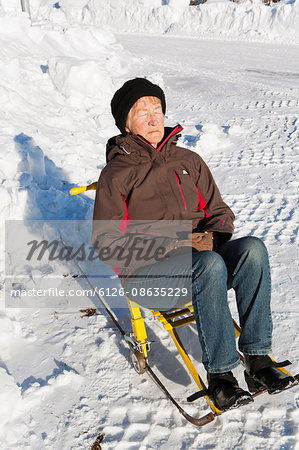 Sweden, Gastrikland, Ockelbo, Woman resting on sleigh in winter sun