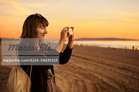 USA, California, Los Angeles, Santa Monica, Mid adult woman photographing at sunset