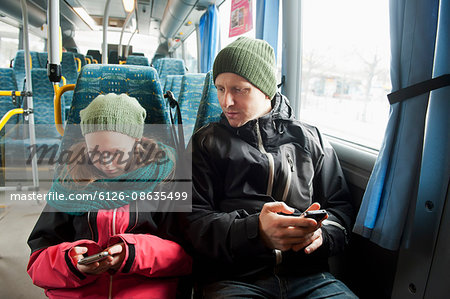 Sweden, Stockholm, Girl (10-11) with father sitting in tram and using smart phones