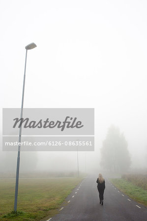 Sweden, Narke, Bjornhammaren, Woman walking along road in fog