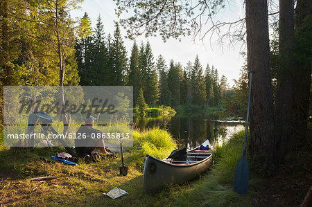 Sweden, Vastmanland, Svartalven, Man sitting by canoe on riverbank