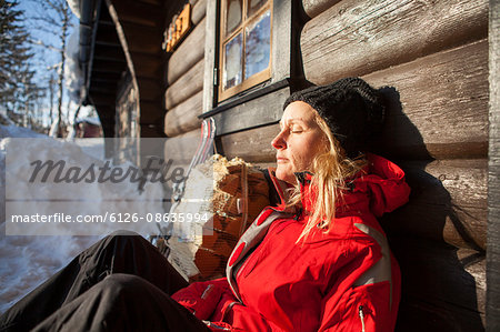 Norway, Trysil, Woman leaning against log cabin