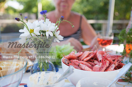 Sweden, Vastergotland, Lerum, Bowl of shrimps and flower vase on table, woman sitting in background