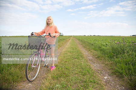 Sweden, Skane, Soderslatt, Beddinge, Blonde girl (10-11) standing with bike on dirt road in green field