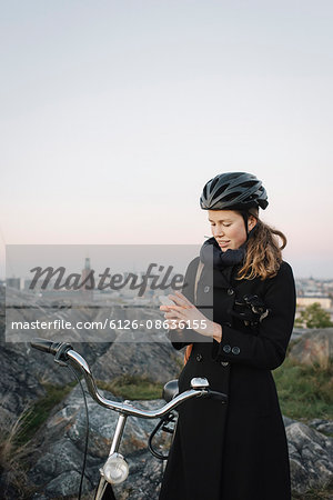 Sweden, Sodermanland, Stockholm, Sodermalm, Skinnarviksberget, Young woman standing by bicycle using phone