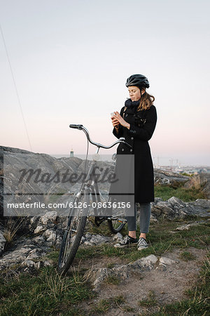 Sweden, Sodermanland, Stockholm, Sodermalm, Skinnarviksberget, Young woman standing by bicycle using phone