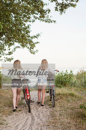 Sweden, Blekinge, Hallevik, Rear view of two teenage girls(14-15, 16-17) walking with bicycles