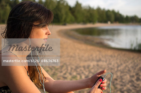 Finland, Pohjanmaa, Pietarsaari, Vanha Satama, Young woman sitting on lakeshore and listening music