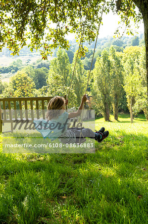 France, Normandy, little girl enjoying a go on a swing in a beautiful countryside garden