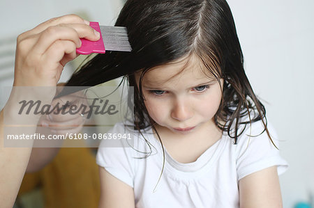 A mother passes a lice comb in the hair of her 6 years old girl