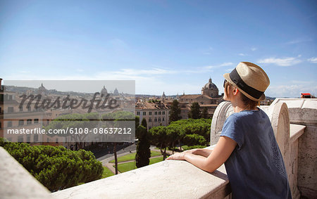 Young woman from behind, leaning on a low wall, and the city of Rome