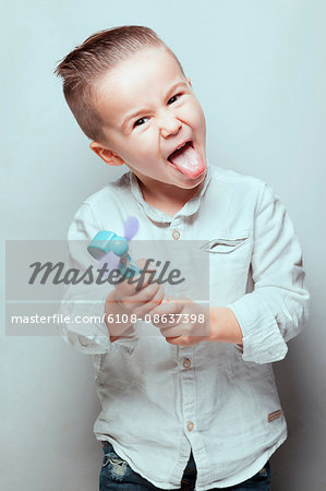 Portrait of a boy sticking his tongue out, a toy in hands