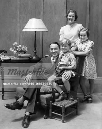 1930s PORTRAIT OF SMILING FAMILY FATHER MOTHER TWO CHILDREN IN LIVING ROOM LOOKING AT CAMERA