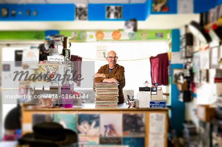 Portrait of mature man in record shop, leaning on stack of records