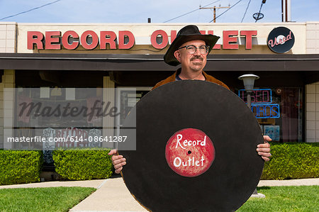 Portrait of mature man outside record shop, holding large imitation record Portrait of mature man outside record shop, holding large imitation record