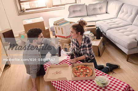 Moving house: Young couple eat pizza in new home, surrounded by boxes