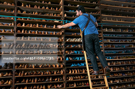 Male cobbler in traditional shoe shop on ladder selecting shoe last