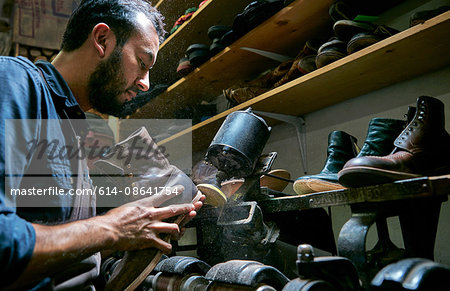 Male cobbler in traditional shoe workshop repairing boot heel