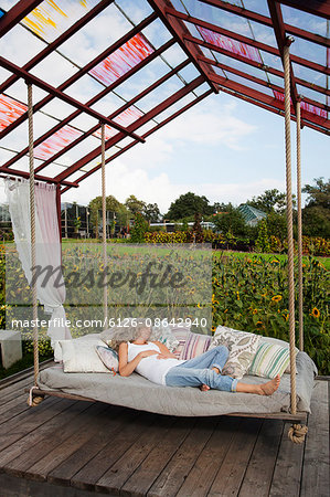 Sweden, Uppland, Solna, Ulriksdal, Woman sleeping on swing in Ulriksdals Handelstradgard