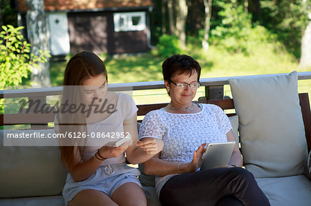 Sweden, Sodermanland, Mature woman using digital table and teenage girl  (14-15) using smart phone
