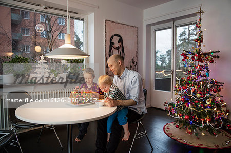 Sweden, Man and two boys (18-23 months, 4-5) decorating gingerbread house