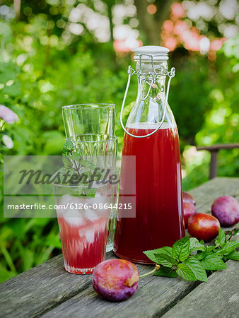 Sweden, Plum juice in glass and carafe, plums and stack of glasses on table