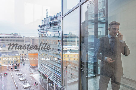 Finland, Helsinki, Businessman seeing through window talking by phone
