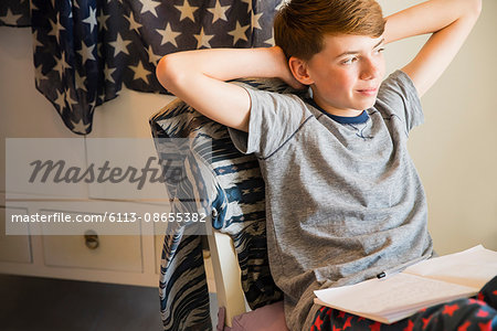 Confident boy doing homework with hands behind head