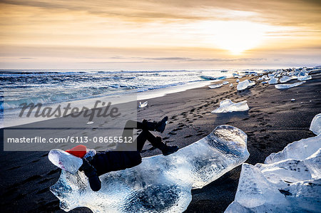 Woman laying on large ice chunk on beach at sunset, Iceland Woman laying on large ice chunk on beach at sunset, Iceland