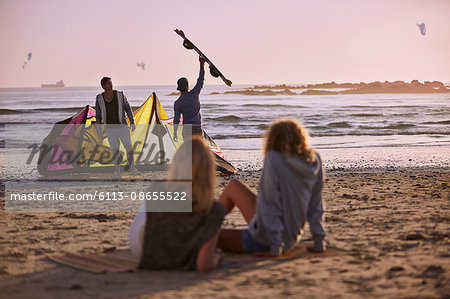 Women watching men preparing to kiteboard on beach