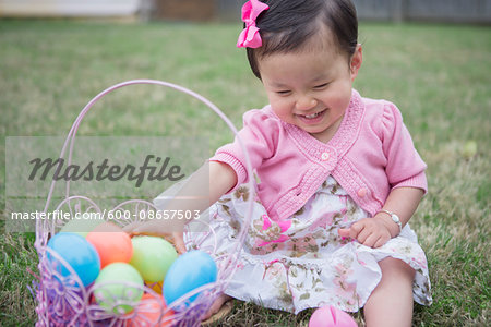 Portrait of Toddler Girl wearing Pink and Sitting on Grass with Easter Basket in Backyard