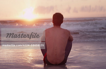Pensive young man on beach watching sunset over ocean Pensive young man on beach watching sunset over ocean