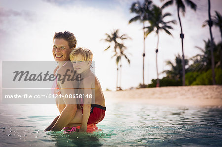 Portrait smiling mother piggybacking son in tropical ocean