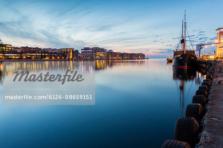 Sweden, Skane, Malmo, Moored ship and cityscape at dusk