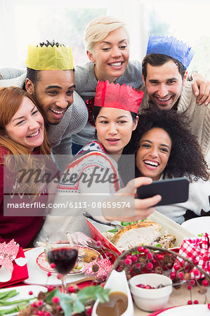 Friends in paper crowns taking selfie at Christmas dinner