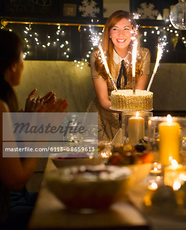 Enthusiastic woman serving cake with sparkler fireworks to clapping friends