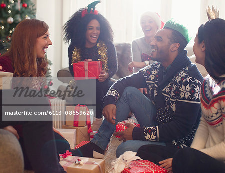 Laughing friends opening Christmas gifts in living room