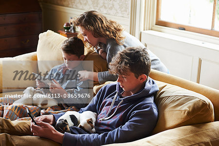 Brothers and sister using digital tablet and cell phone with puppies in laps