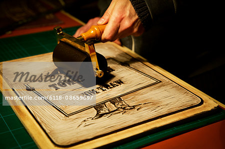 A sign maker rolling ink across the cut raised surface of linoleum preparing to print.