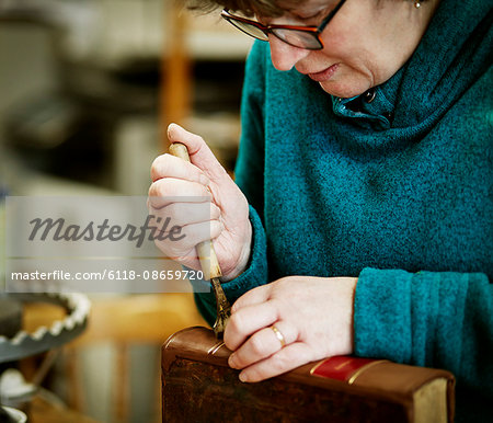 A woman working on the spine of a bound book with a hand tool.