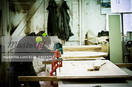 A woman working in a furniture maker's workshop cutting timber with a saw.